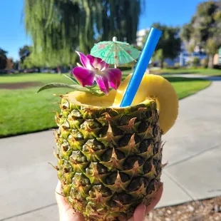 a person holding a pineapple with a straw and a blue umbrella