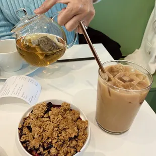 Side bowl of granola and berries, iced lavender latte and the &quot;Blessings&quot; tea in a teapot.