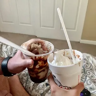 a person holding two cups of ice cream and a spoon