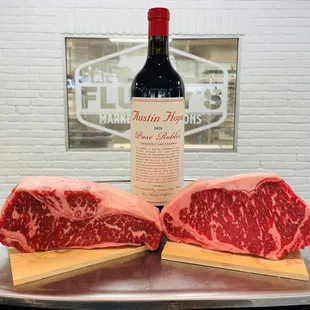 two raw steaks on a cutting board with a bottle of wine in the background