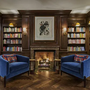 two chairs in front of a fireplace in a library