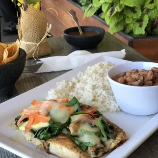 Chicken breast with veggies and melted cheese with a side of whole beans and withe rice