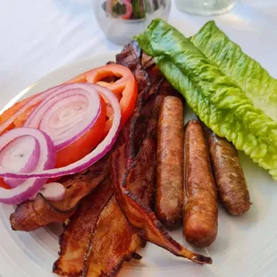 a plate of bacon, lettuce, tomatoes, and sausages