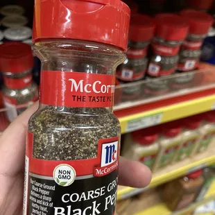 a hand holding a jar of black pepper
