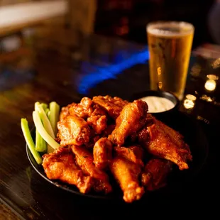 a plate of chicken wings and celery with a pint of beer in the background