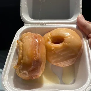 two glazed donuts in a styrofoam container