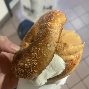 a person holding a bagel with peanut butter on it