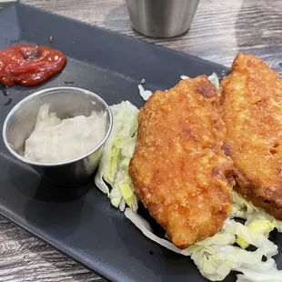 two pieces of fried fish on a bed of lettuce with a side of ketchup