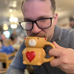 a man holding a coffee mug with a teddy bear on it
