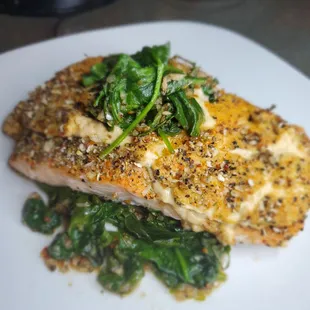 a piece of fish with spinach on a white plate