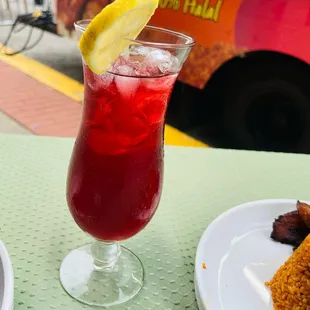 a glass of red drink with a lemon wedge