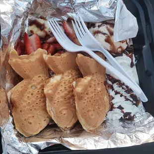 Taiyaki fish-shaped waffles filled with cheesecake and Nutella, with a side of ice cream and fruit.