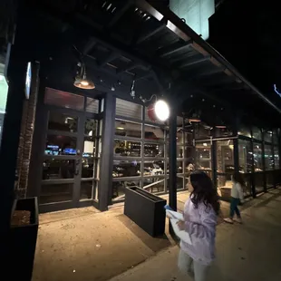 a woman walking down a sidewalk at night