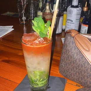 a tall glass of cocktail with a straw and mint