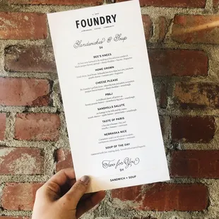a hand holding a menu in front of a brick wall