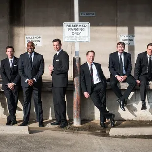 a group of men in suits sitting on a wall