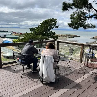 two people sitting at a table on a deck overlooking the ocean