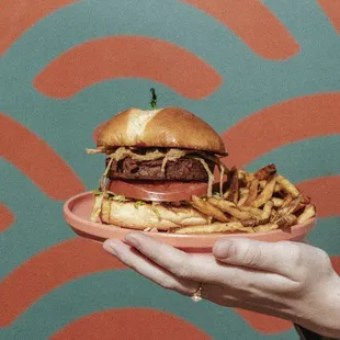 a hand holding a plate with a hamburger and fries
