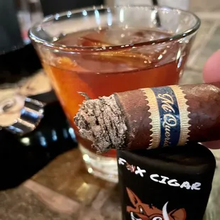 a hand holding a cigar and a glass of tea