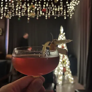 a person holding a cocktail in front of a christmas tree