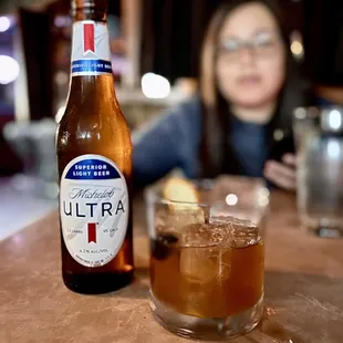 a woman sitting at a bar with a bottle of ultra