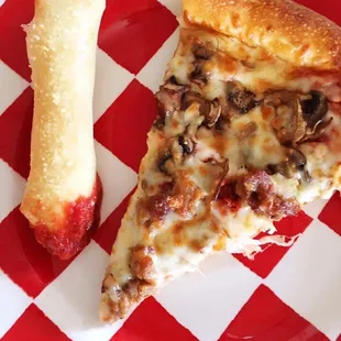 Slice of sausage mushroom pizza with one of their breadsticks dipped in marinara.