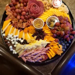 a platter of cheese, meat, grapes, and crackers