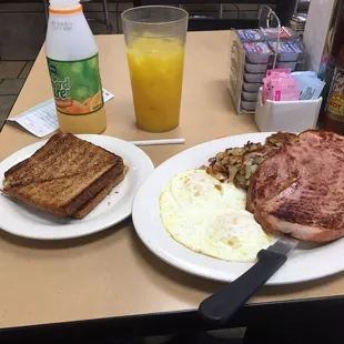 Two egg breakfast with hash browns, grits, eggs over medium, wheat toast, and orange juice