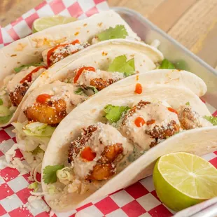 Our shrimp tacos are served on a warm bed of flour tortillas, topped with  cabbage, cilantro, lime, queso crumble,  red onion, sriracha