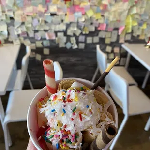 a hand holding a cup of ice cream with sprinkles and sprinkles