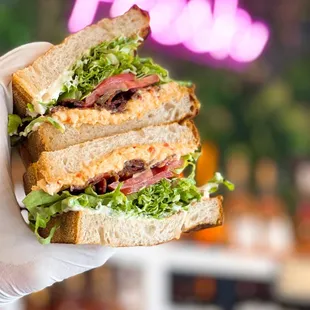 a hand holding a sandwich with lettuce and meat