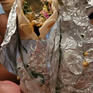 a person holding a pita wrapped in aluminum foil