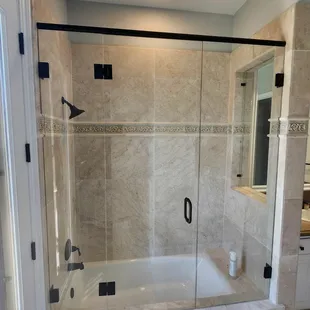 Custom frameless shower door with a stationary panel inside the window opening.