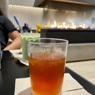 Iced black tea with honey, and an iced matcha latte with vanilla. both are in glasses with a fireplace in the background!