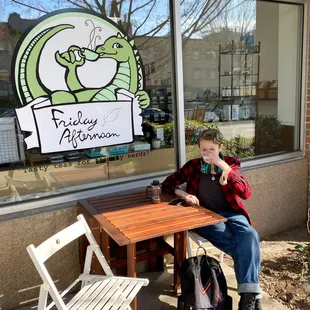 A teenager sips tea at an outdoor table in front of a tea shop.