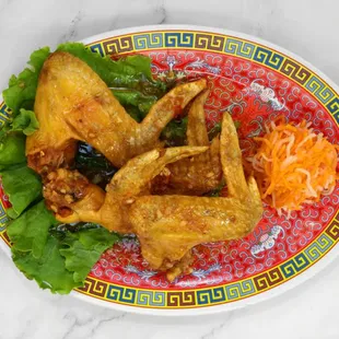 a plate of fried chicken wings with lettuce and carrots