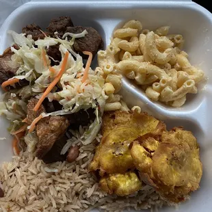 Griot, fried green plantain, rice and peas, macaroni salad and pikliz.