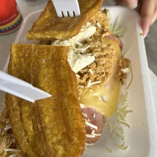 Some kind of sandwich with fried plantains , cheese, lettuce and ham