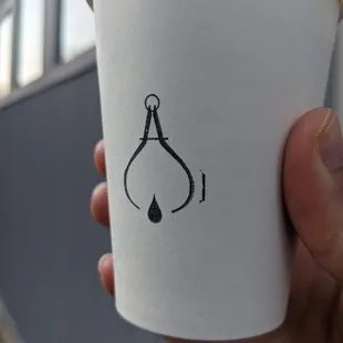 a hand holding a paper cup with a drawing of a hook on it