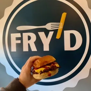 a person holding a sandwich in front of a fry d sign