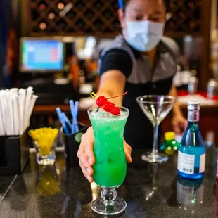 a bartender in a face mask preparing a cocktail