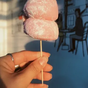 a person holding a pink donut on a stick