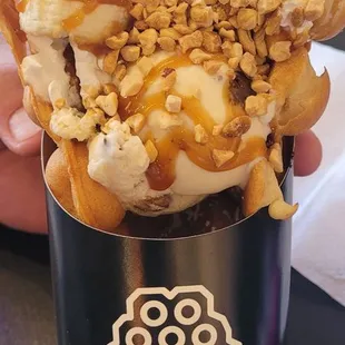 a hand holding a cup of ice cream and caramel