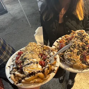 a woman holding two plates of funnel cake