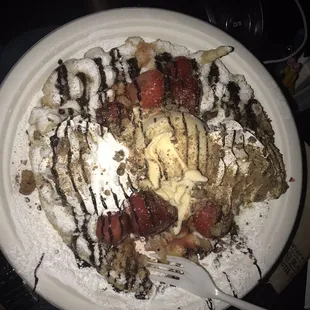 Funnel cake with vanilla ice cream, whipped cream, strawberries, chocolate drizzle.
