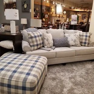Linen colored sofa shown with matching accent ottoman. Throw pillows are included, and the plaid pillows match the ottoman.