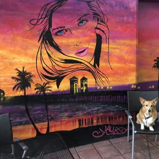 a dog sitting on a chair in front of a mural