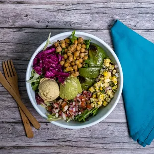 a bowl of salad with a blue napkin and wooden utensils