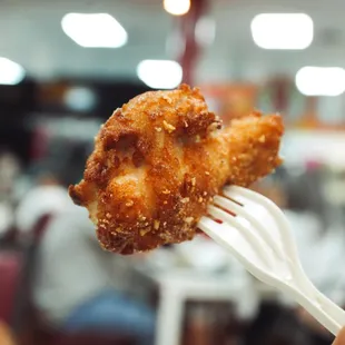 a hand holding a piece of fried chicken on a fork