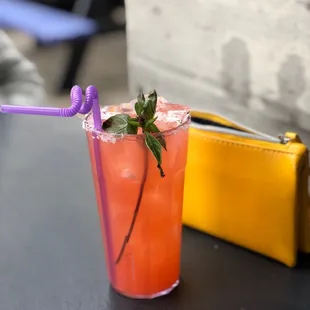 a drink in a tall glass with a straw and a purple straw with a sprig of mint